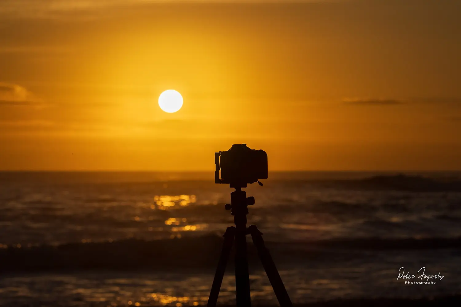 Silhouette of a camera on a tripod capturing a golden sunrise over the ocean