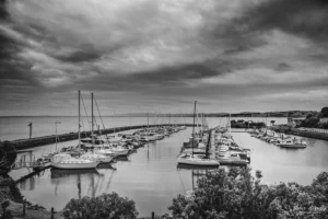 Black and white photograph of yachts moored at a marina on Phillip Island under dramatic clouds